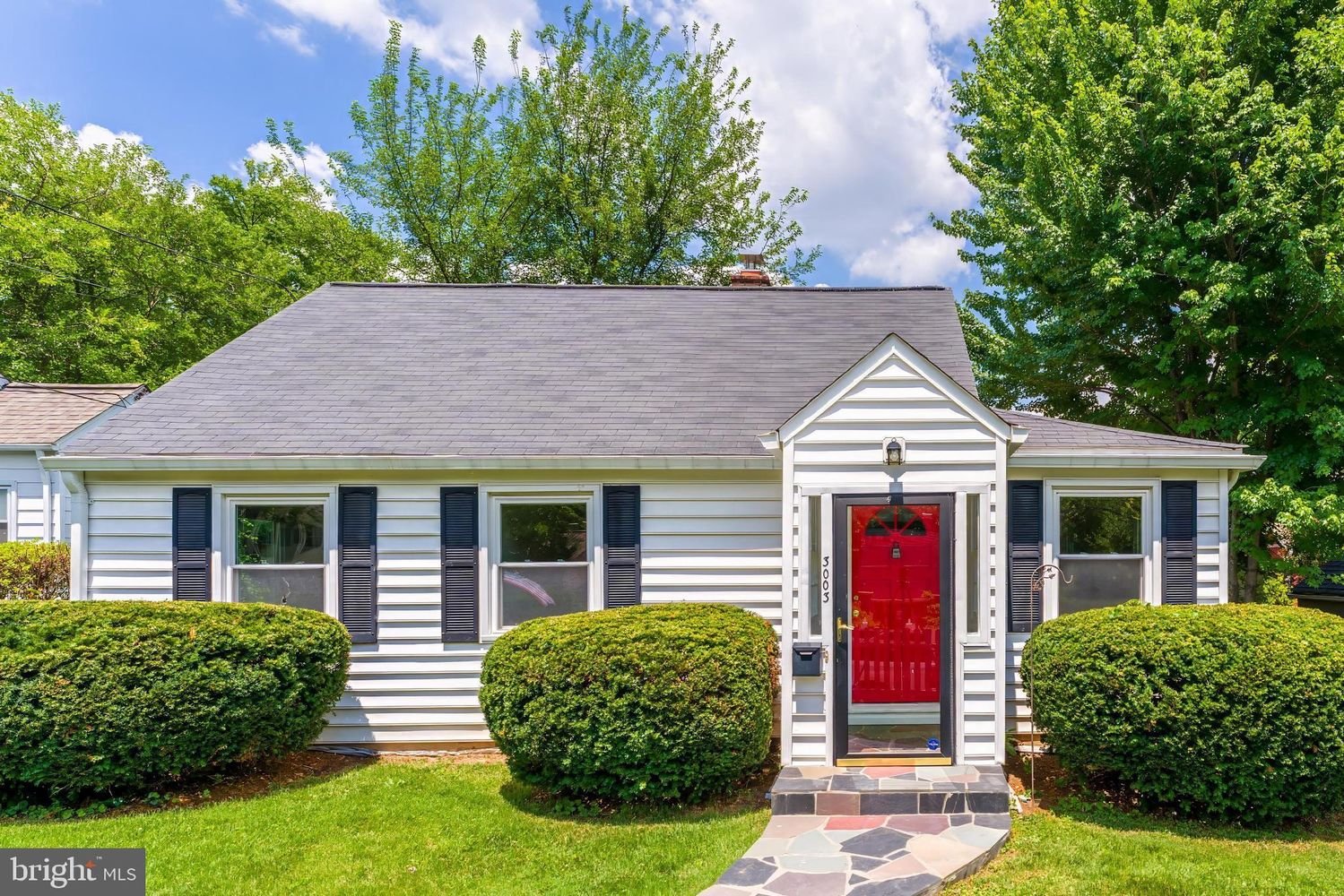 A charming single-story house with white siding, black shutters, and a vibrant red front door in a suburban neighborhood.