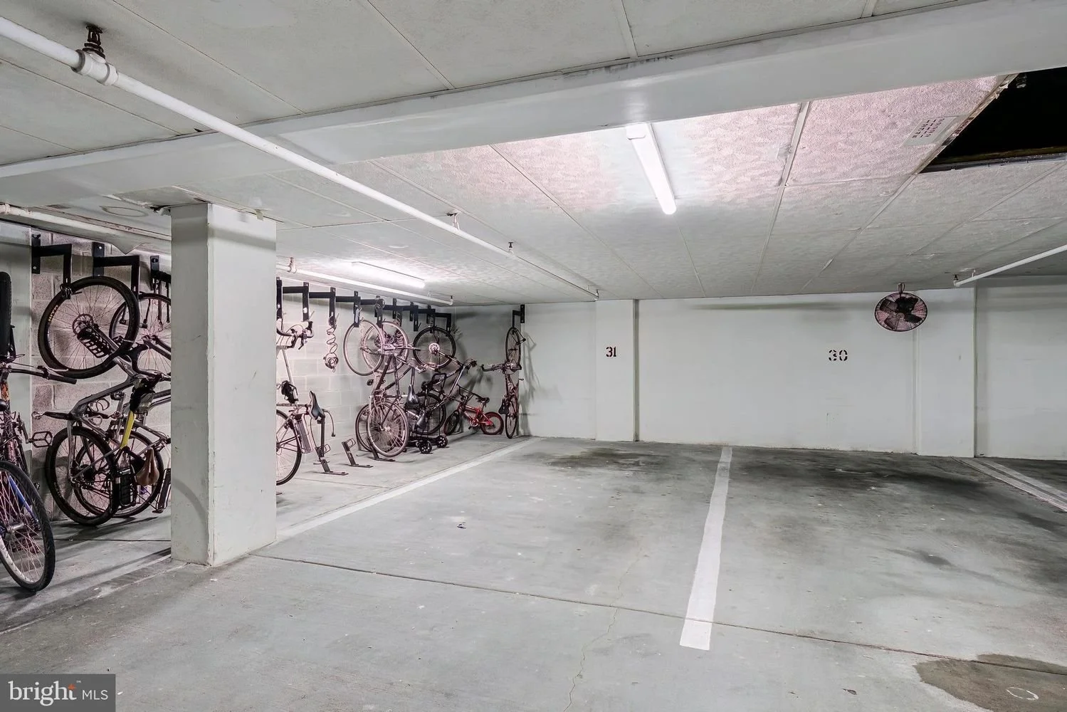 Underground parking lot with four parking spaces numbered 30 and 31, some bikes parked on the left side, a vent and a ceiling fan visible.
