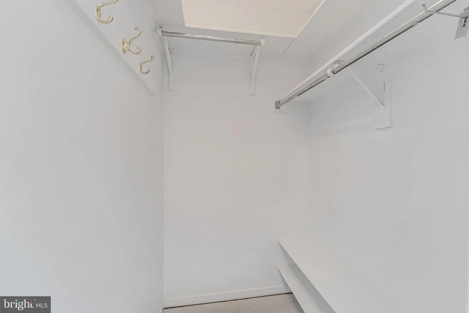Empty walk-in closet with white walls, two hanging rods, and three hooks on the wall.
