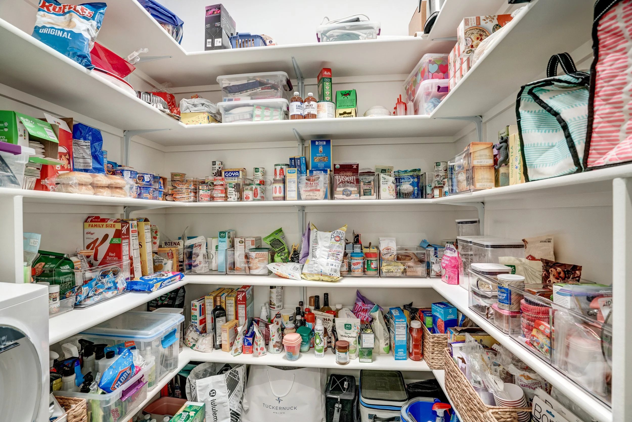 An organized pantry with three shelves filled with various food items, containers, boxes, and snacks, with some empty space for storage.