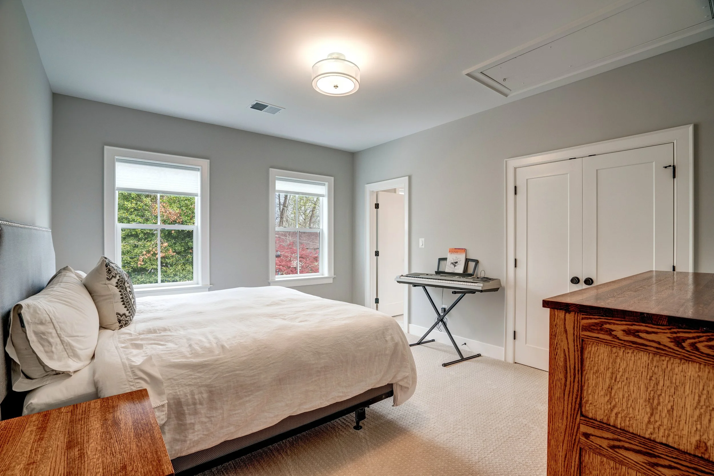 A bedroom with a bed, window view of trees, a keyboard, and a wooden dresser.