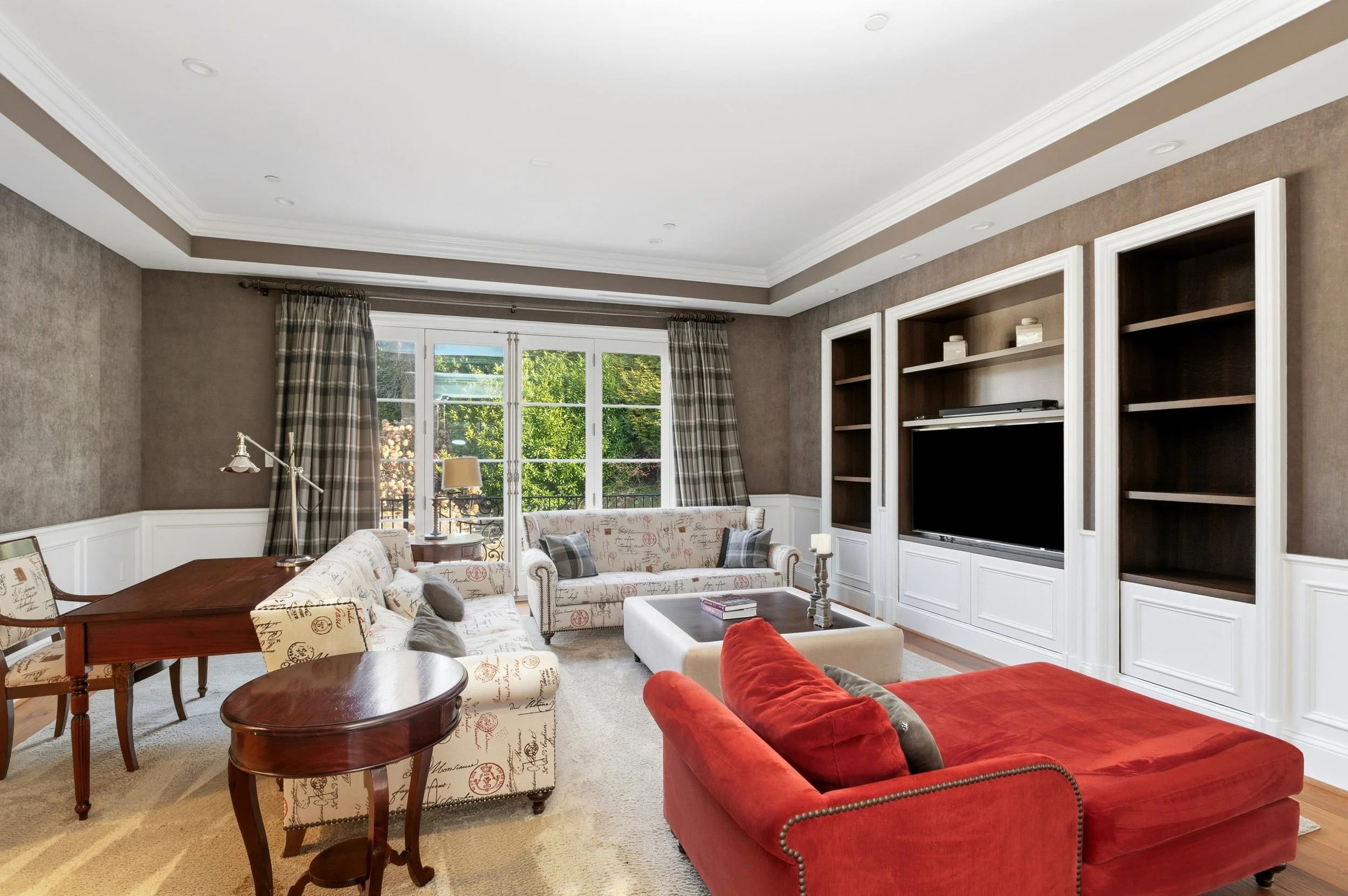 Living room with a large window, beige carpet, multiple sofas, and built-in bookshelves with a TV.
