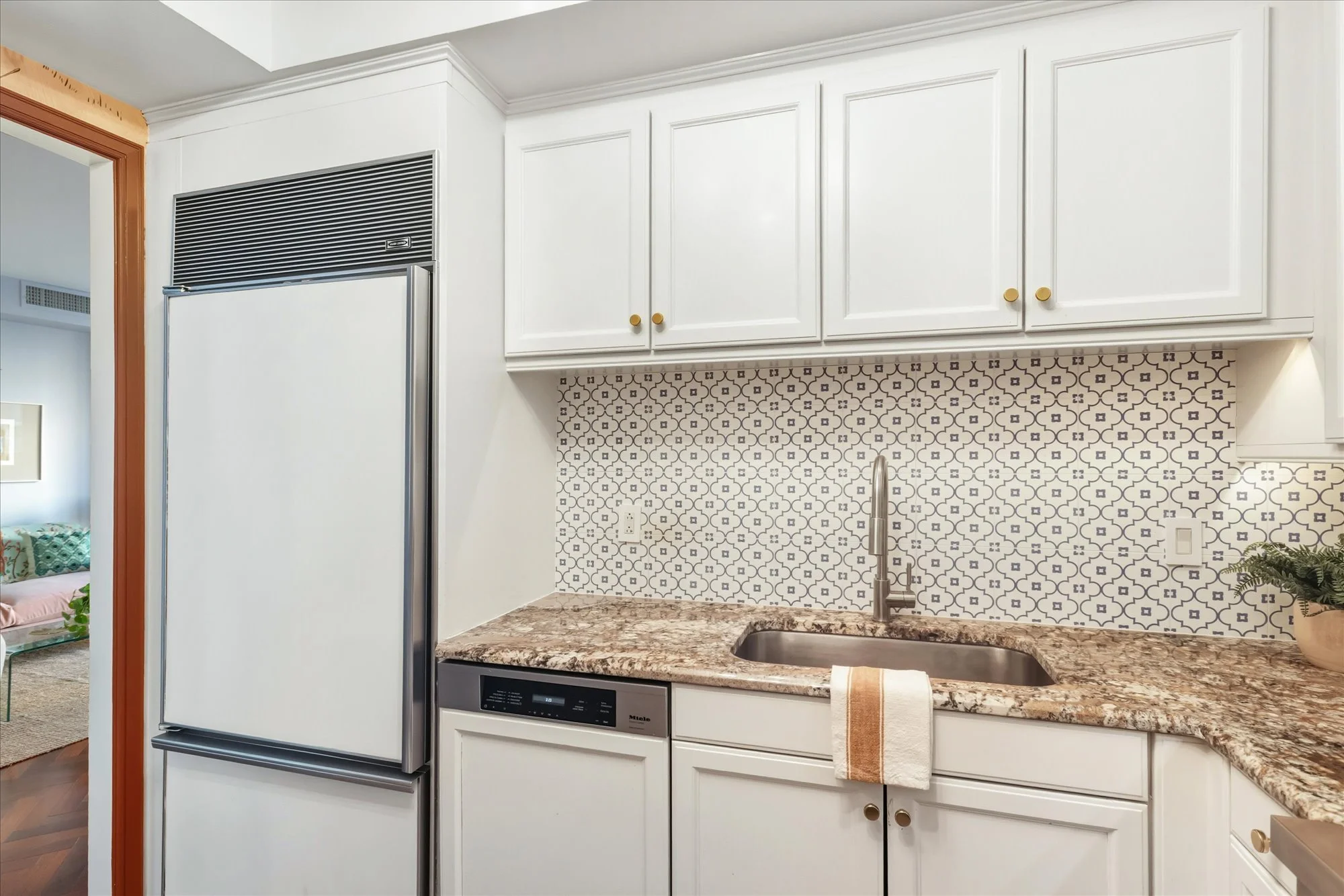 A modern kitchen with white cabinets, a patterned tile backsplash, marble countertop, and stainless steel sink.