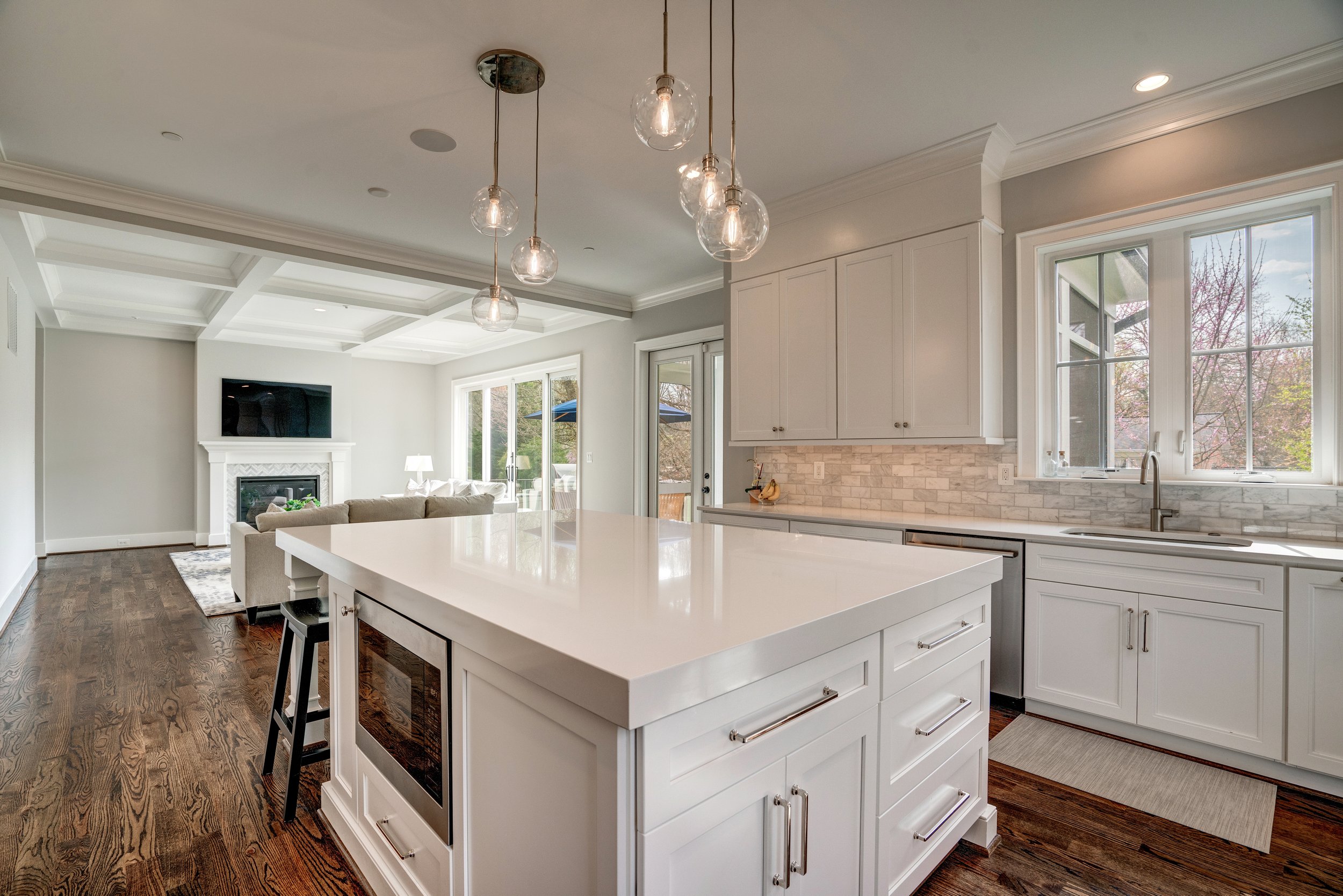Modern kitchen with white cabinets, a central island, pendant lights, and large windows providing natural light.