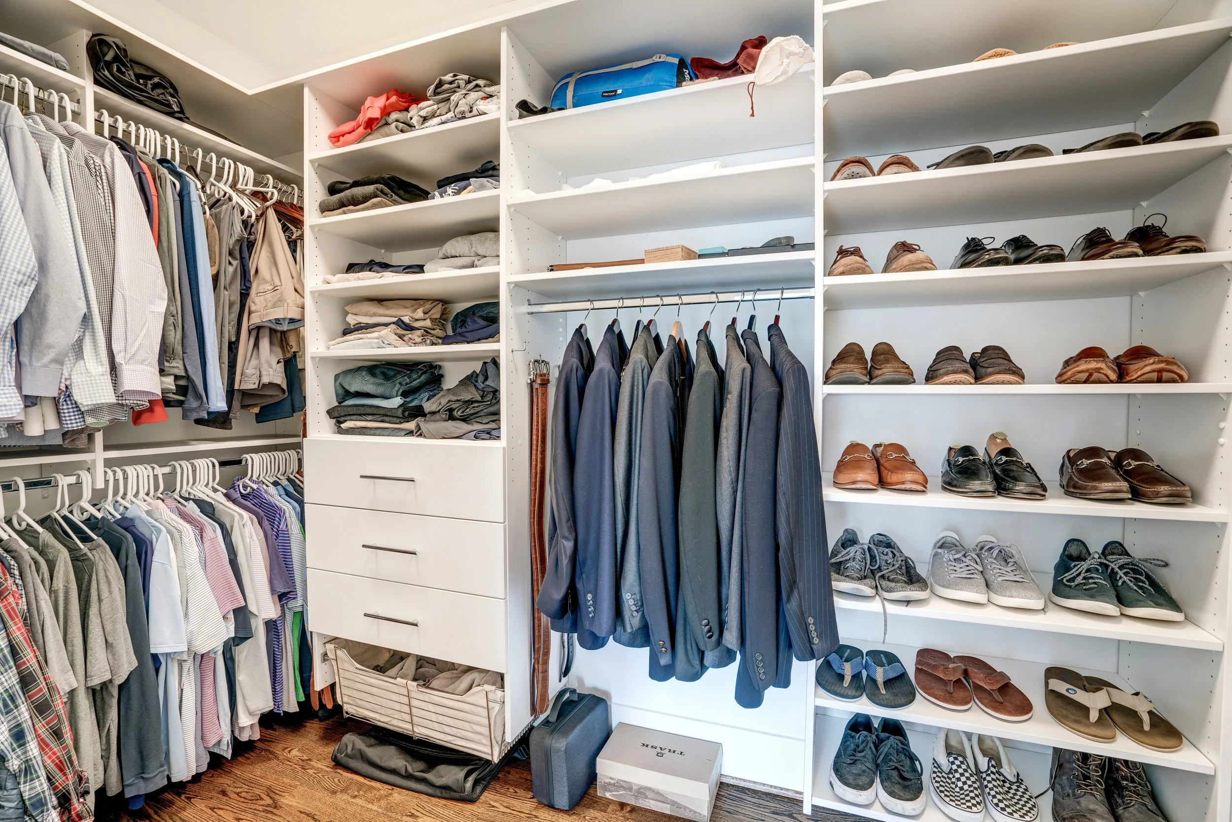 Organized walk-in closet with shelves and hanging rods filled with clothes, shoes, and accessories.