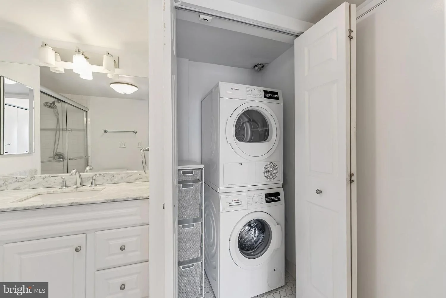 Stacked washer and dryer in a small laundry closet with a metal storage cart to the side.