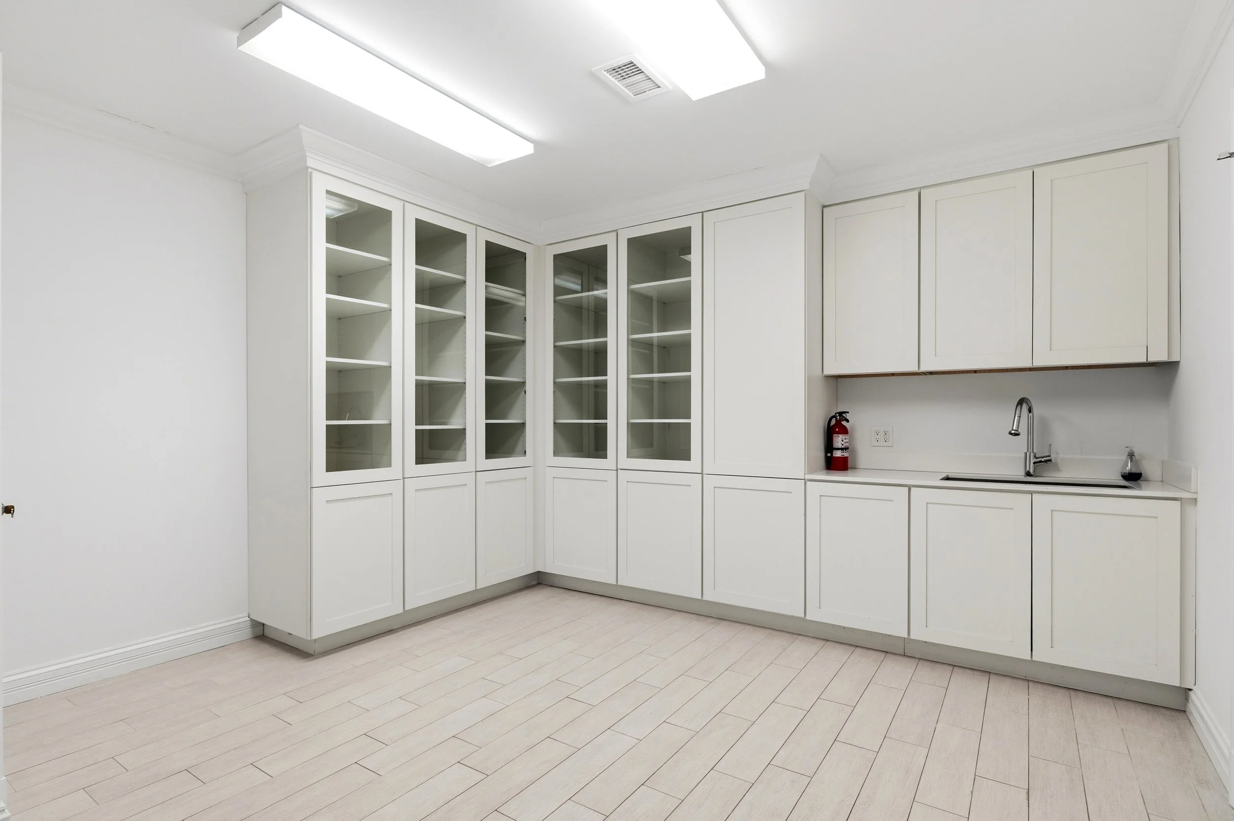 Empty white kitchen with built-in cabinets, a sink, and fire extinguisher.