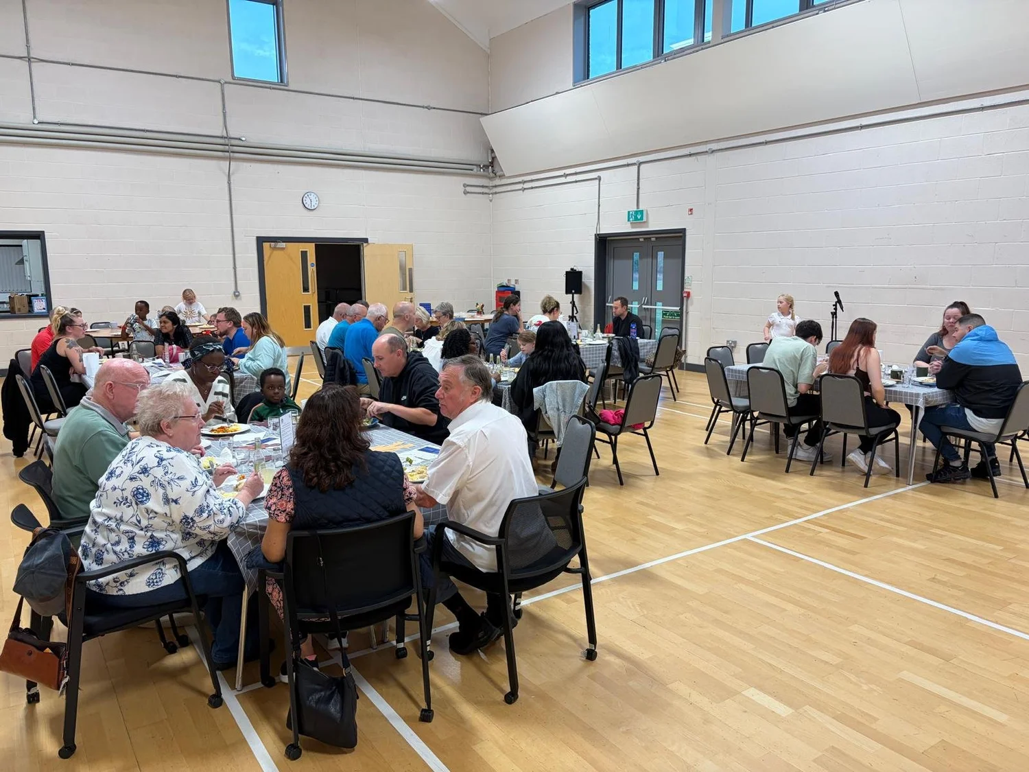 Neighbours, families and children sharing a meal around tables at The Table in Marston Moretaine Community Centre