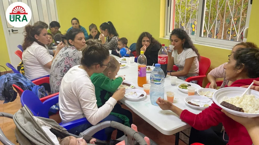 Families eating together around a long table at the Tek Ura centre