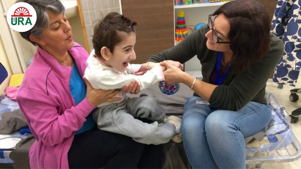 A physiotherapist and a mother working with a young child in the Tek Ura rehab clinic