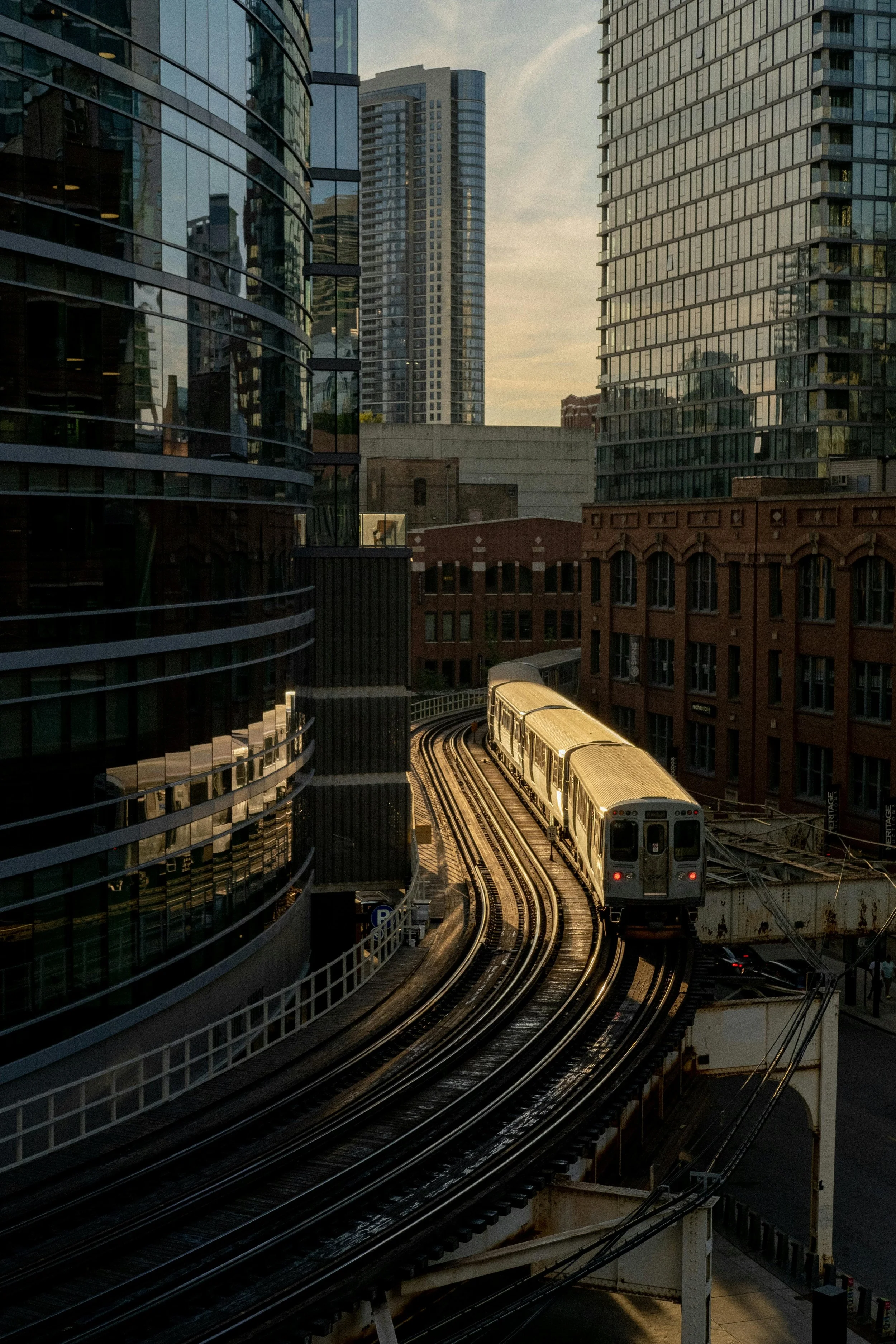 A cityscape featuring modern glass buildings and an elevated train moving on tracks through the urban area during sunset.