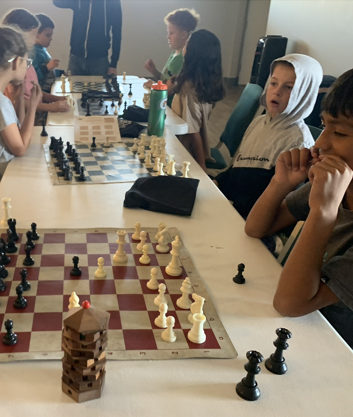 Children playing chess at a long table in a room.