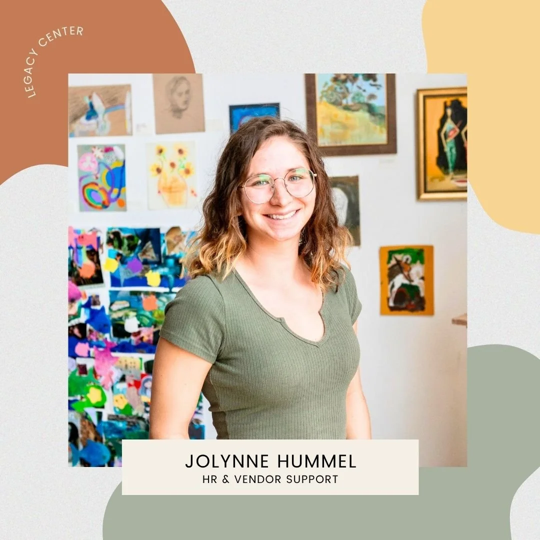 A woman with glasses and shoulder-length wavy hair smiling, standing in front of an art display wall with various colorful paintings. She is wearing a green ribbed t-shirt. The text on the image reads "Jolynne Hummel, HR & Vendor Support" and a label in the top left corner says "Legacy Center."
