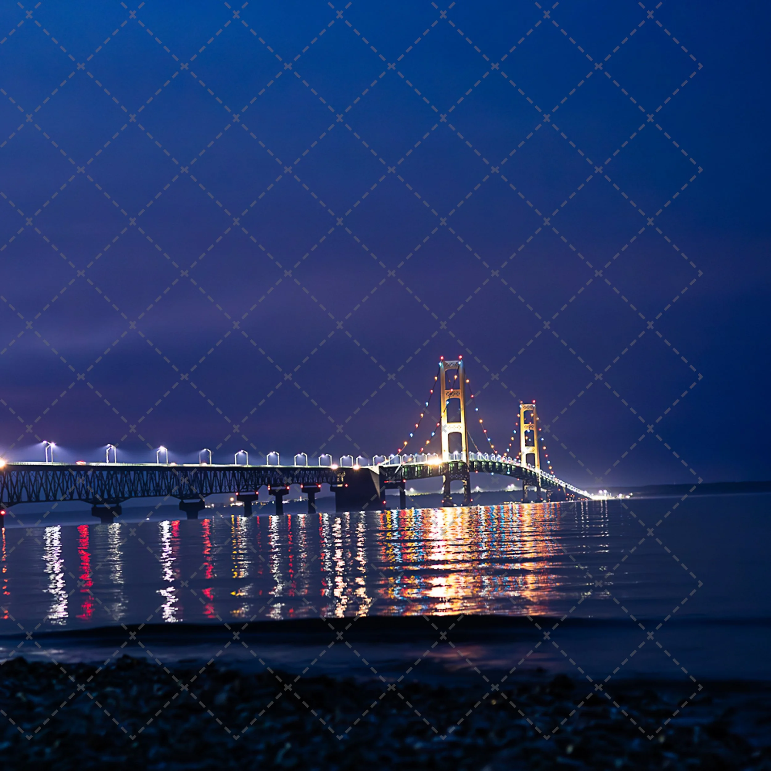 Night view of a bridge with illuminated towers reflecting on water.
