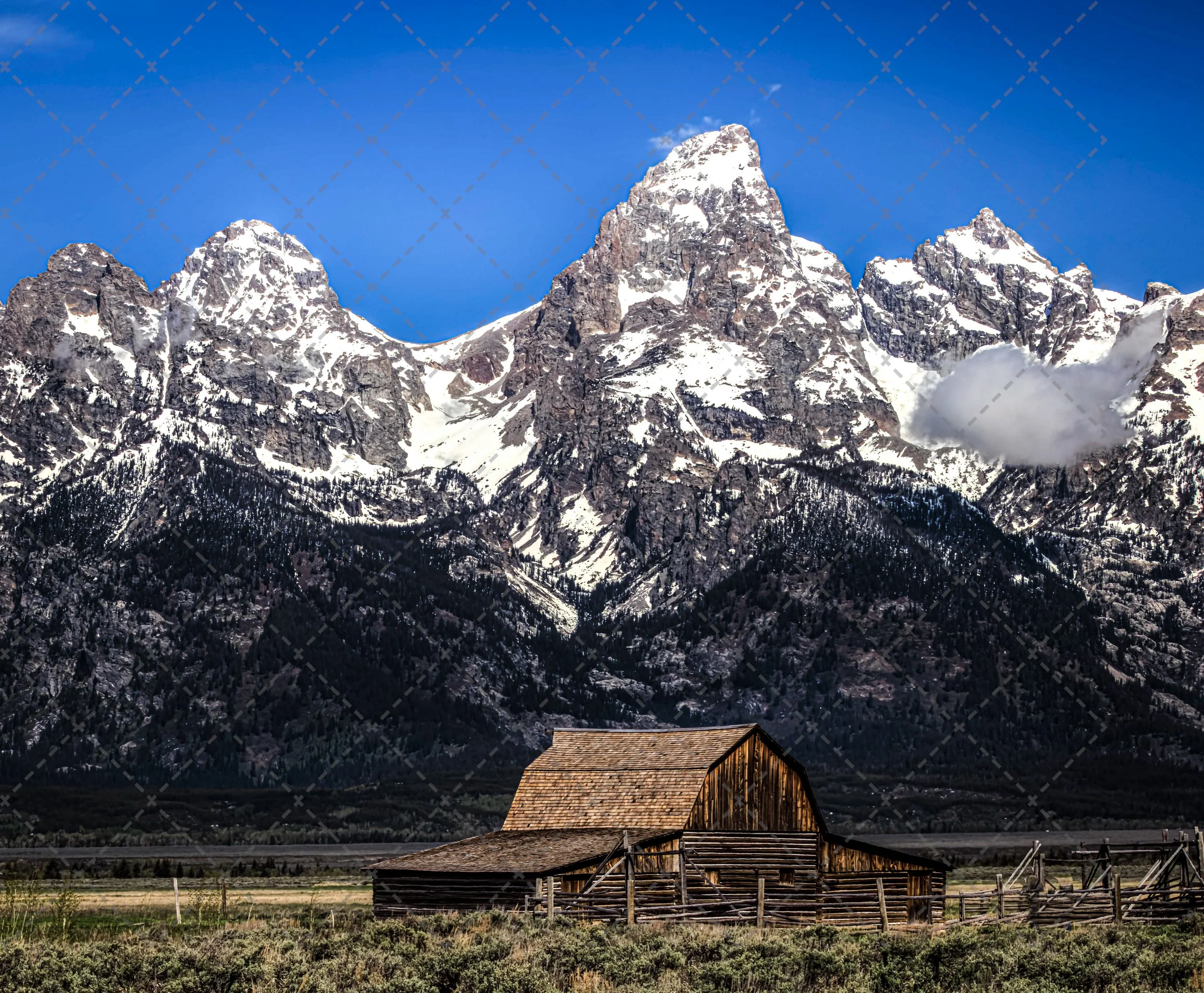 Scenic view of snow-capped mountains under a clear blue sky with a small wooden barn in the foreground.