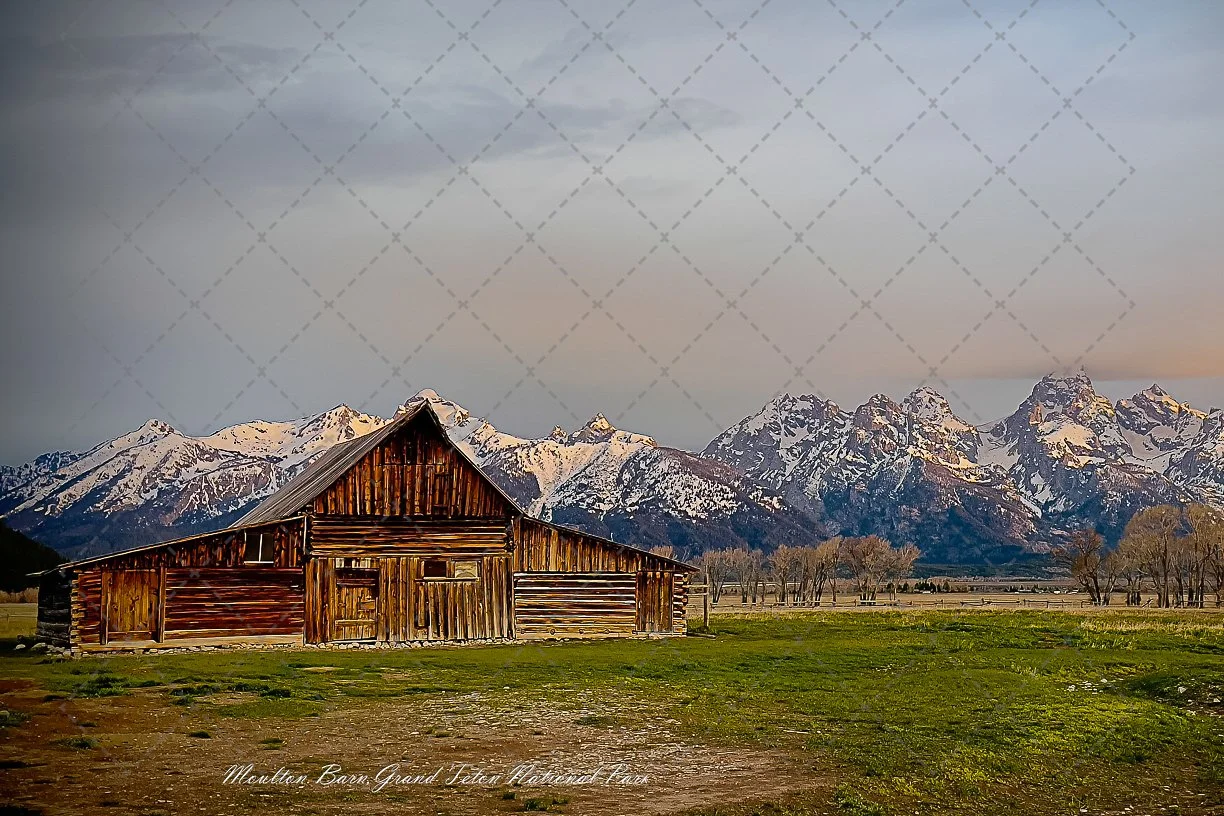 A wooden barn with mountains in the background and a partly cloudy sky.
