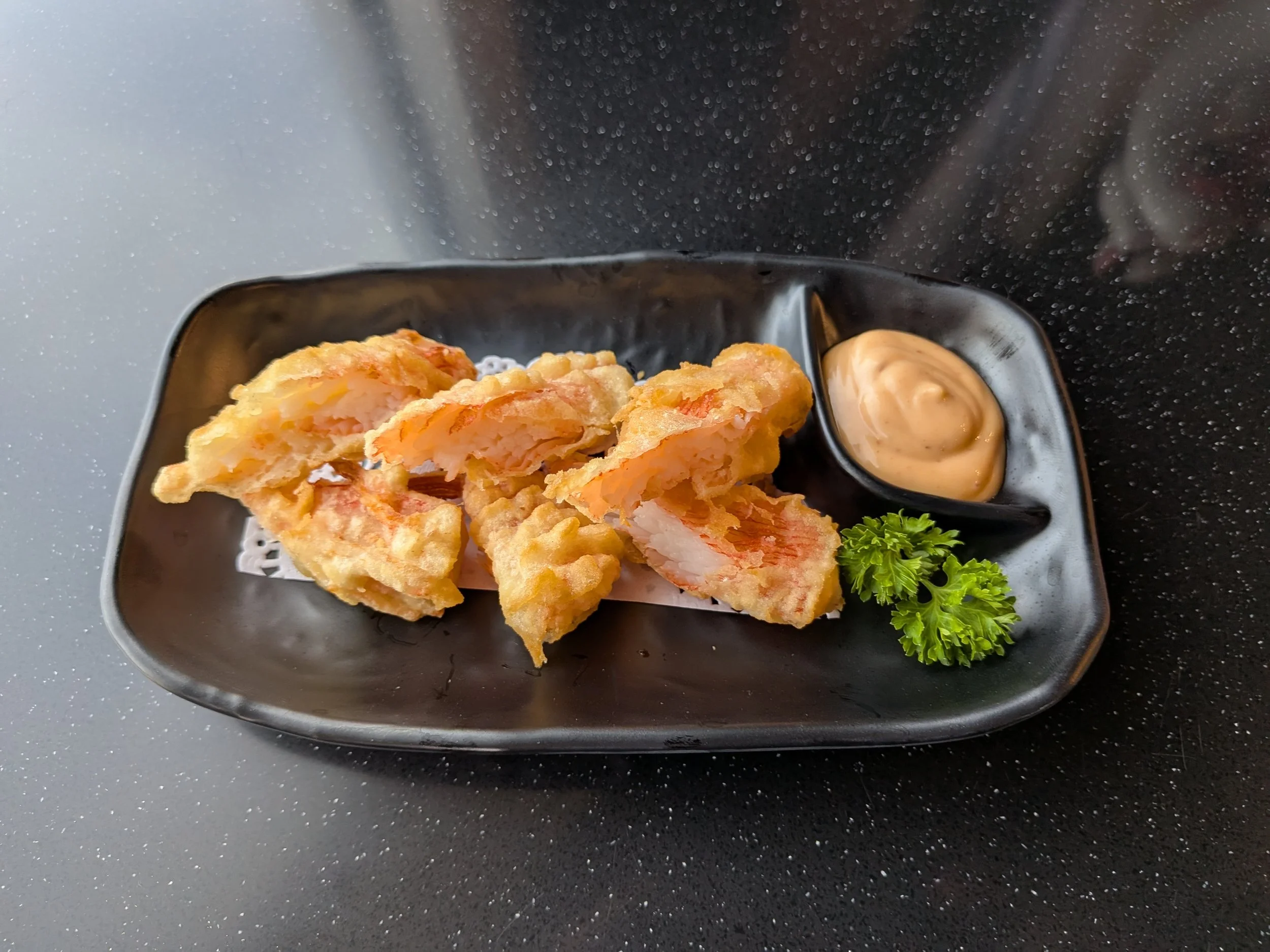 Close-up of fried fish fillets with tartar sauce and garnish on a black tray.