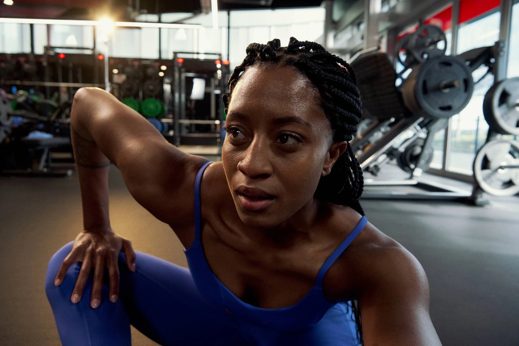 Woman in blue workout attire stretching in a gym with weightlifting equipment in the background.
