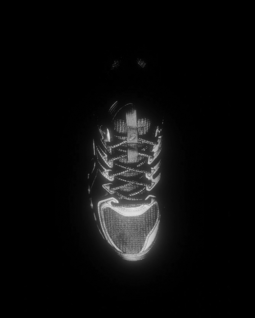 Black and white image of an Asics sneaker illuminated with LED lights, viewed from above in darkness.