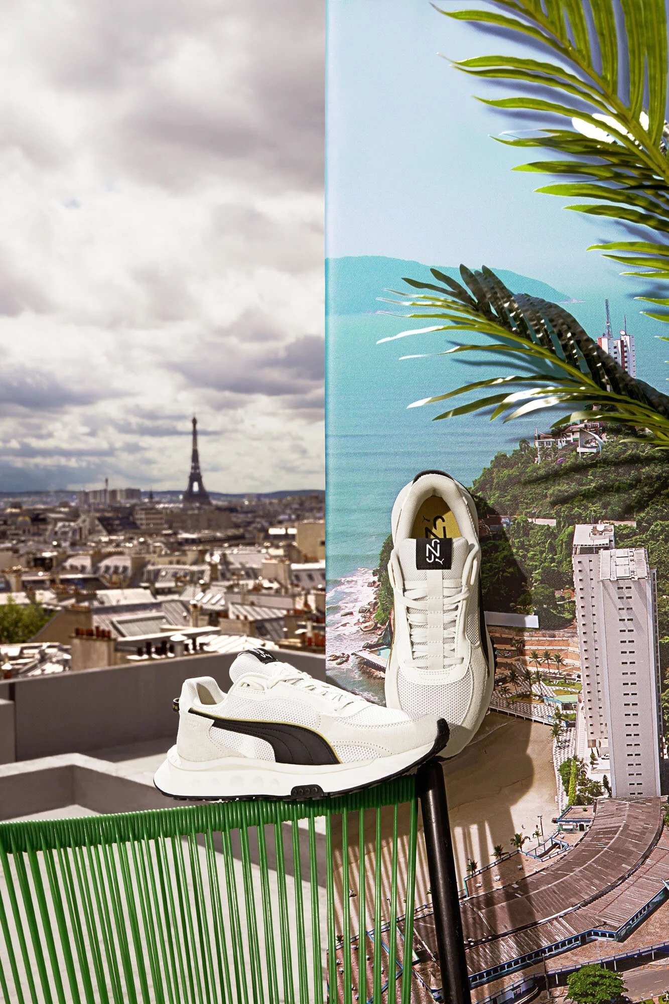 A pair of white athletic shoes resting on a rooftop ledge with Paris skyline and a mural of a tropical beach scene on the wall behind, including the Eiffel Tower in the distance, palm trees, and ocean waters.