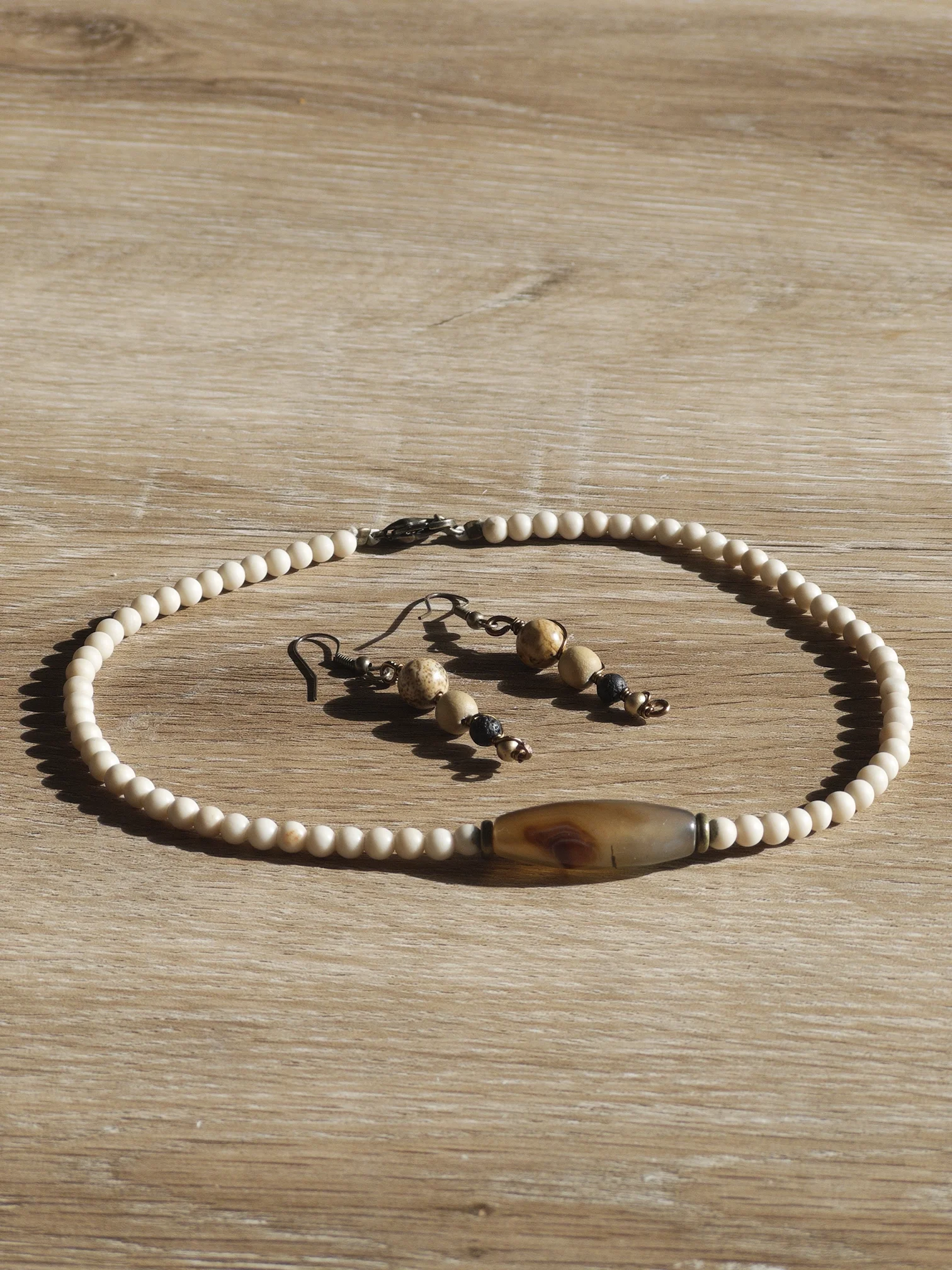 A close-up of a pearl necklace and matching earrings on a wooden surface, with sunlight casting shadows.