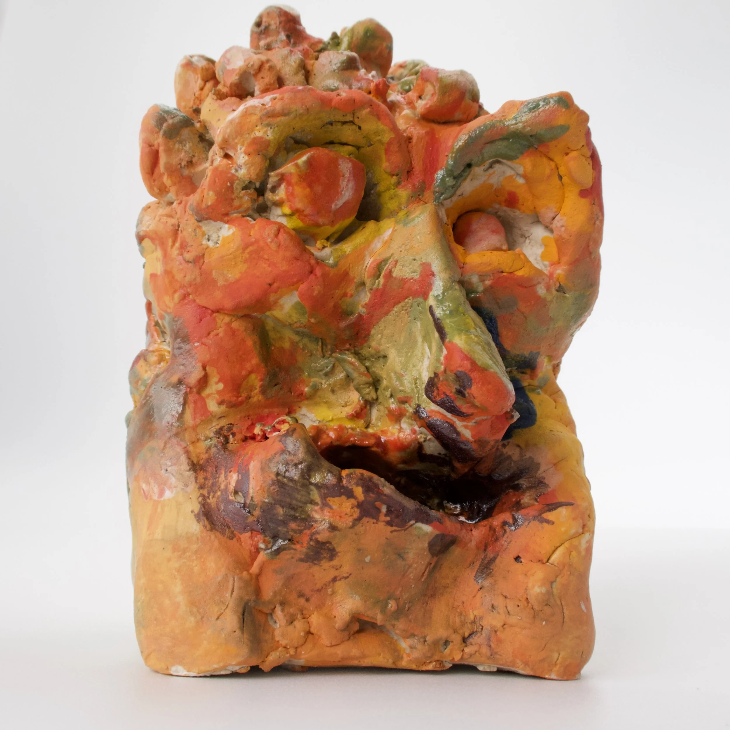 A close-up of a multicolored, textured mineral specimen with orange, yellow, green, white, and black areas, and a rough, irregular surface.