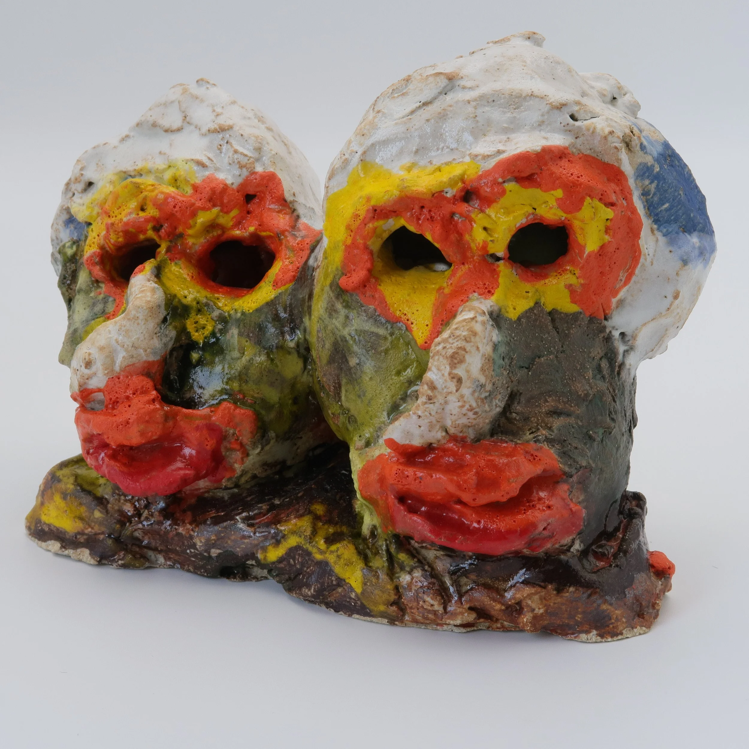 Close-up of a ceramic skull sculpture with colorful painted details, including red, yellow, blue, and black, on a white background.