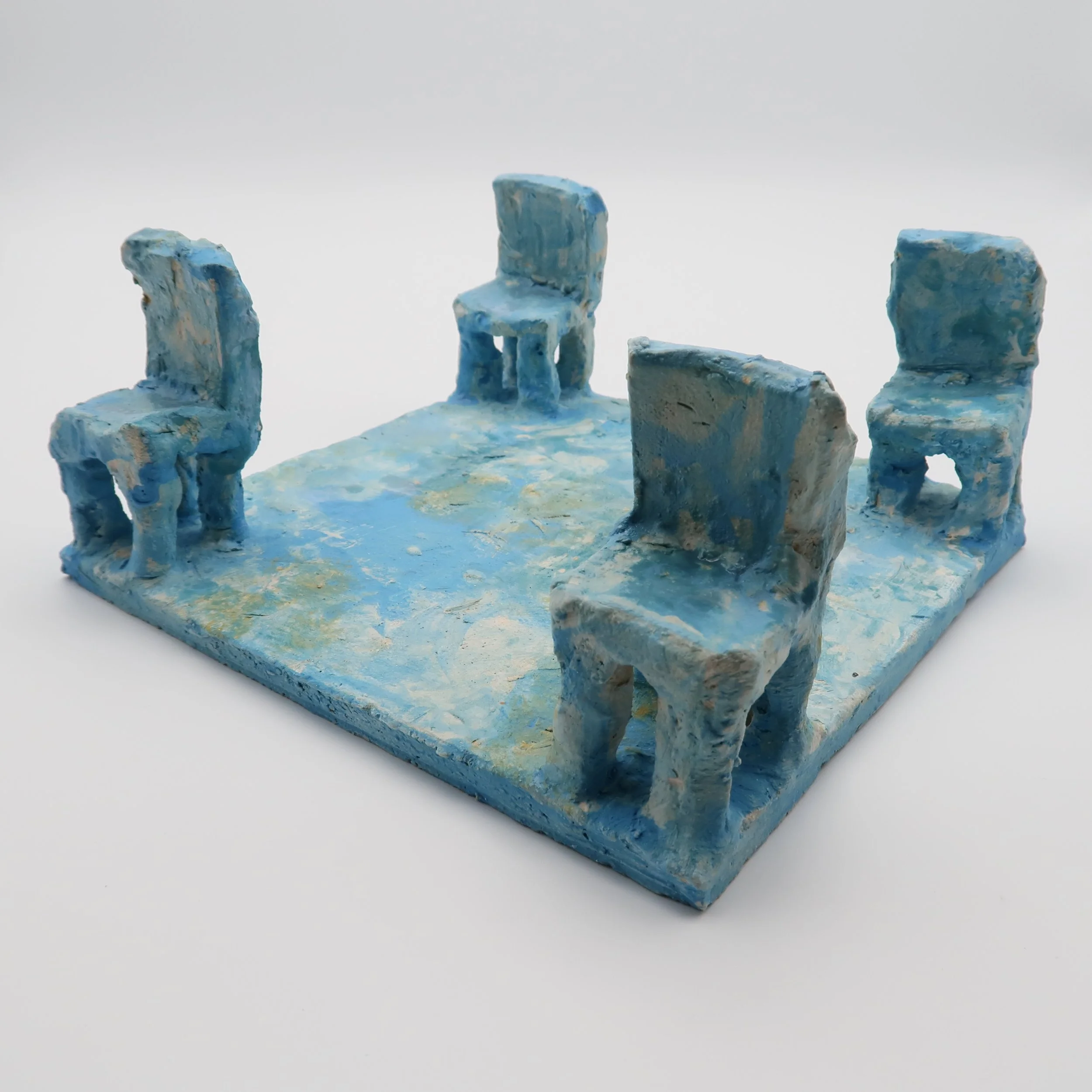 Small blue painted model of the Stonehenge monument with six upright stones and a horizontal lintel stone on top, set against a plain white background.