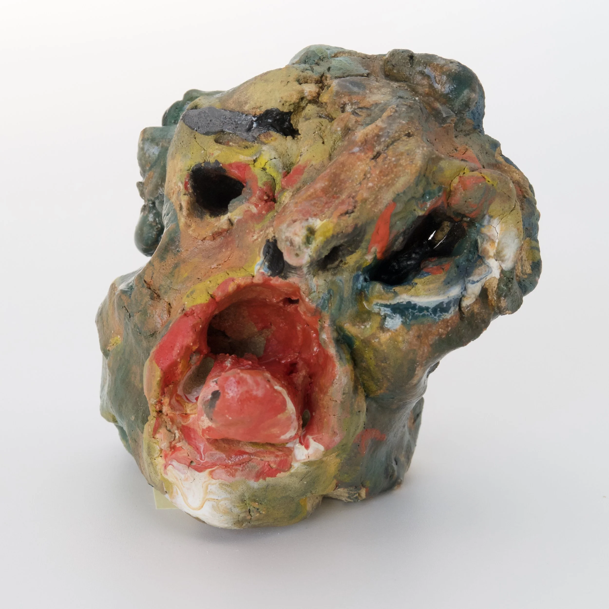 A colorful, textured sculpture resembling a distorted face with open mouth, painted with mixed colors including yellow, red, blue, and black, placed on a white background.