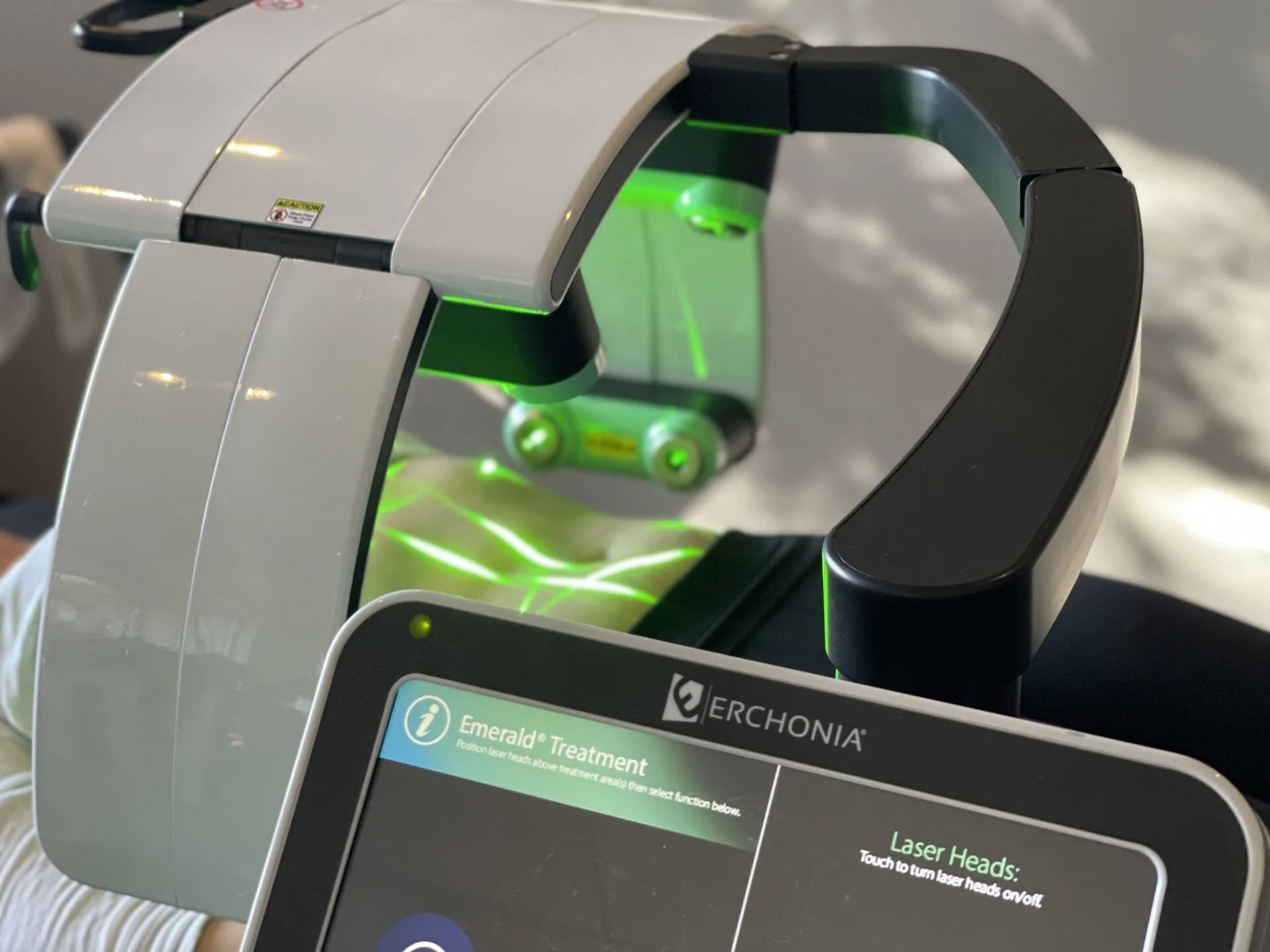 Close-up of the Erchonia Emerald Laser device with green laser light and touchscreen controls used for non-invasive fat reduction treatments.