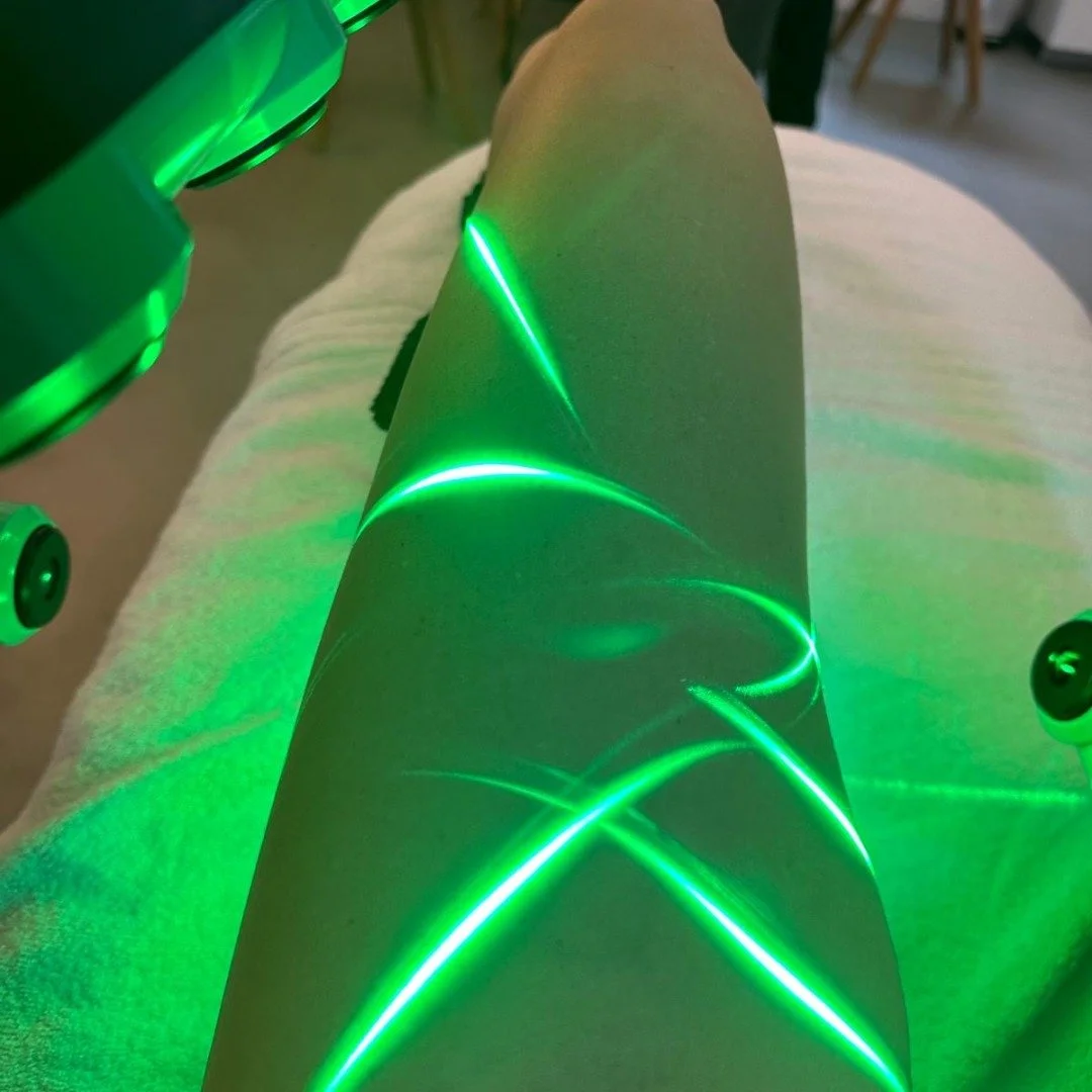 Client receiving Erchonia Emerald Laser therapy on the leg, with green low-level laser light directed at the treatment area.