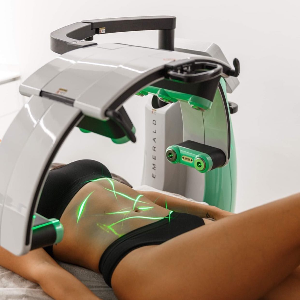 Client lying on a treatment table receiving Erchonia Emerald Laser therapy to the abdomen using green low-level laser light.