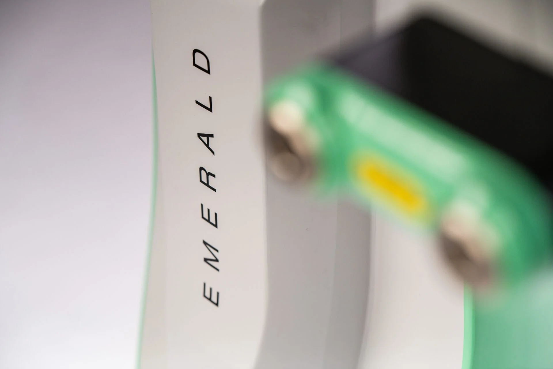 Out-of-focus close-up of the Erchonia Emerald Laser device with Emerald branding visible.