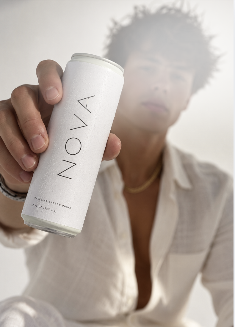 NOVA founder, Sam Schulenburg,  holding a can of NOVA, clean sparkling energy drink toward the camera, with a plain light-colored background.