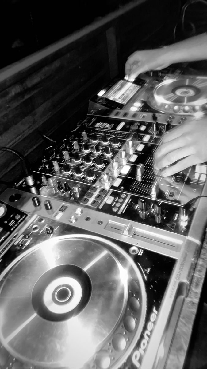 Close-up of a DJ mixing console with hands adjusting controls, in a dimly lit environment.