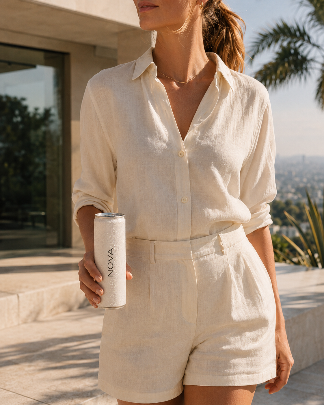 A woman wearing a cream-colored button-up shirt and matching shorts holding a white can with the brand name 'NOVA' on it, standing outdoors on a sunny day with buildings and palm trees in the background.