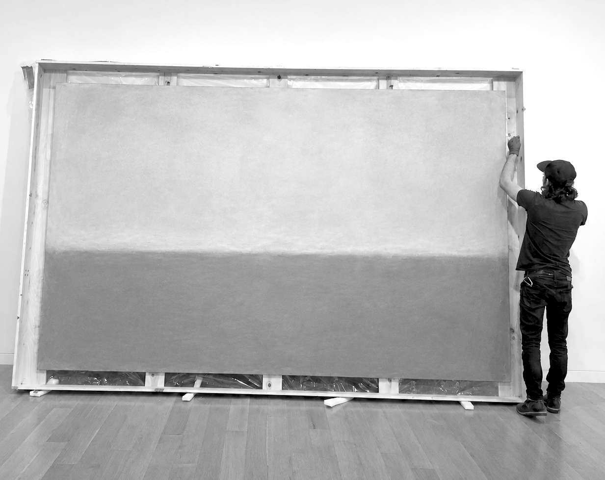 Person installing or assembling a large framed artwork or display on a white wall in an indoor space.