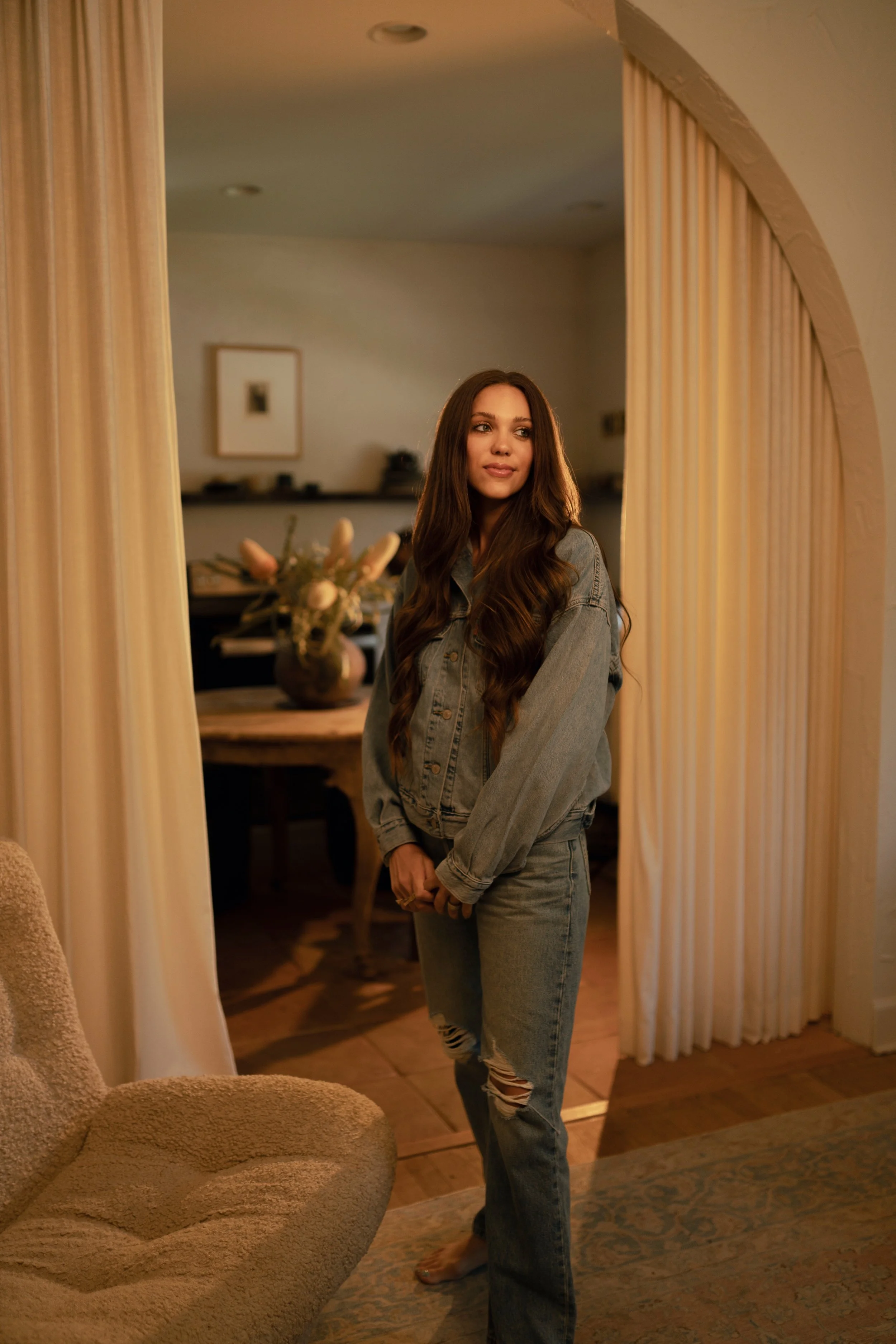 woman wearing a denin-on-denim outfit with an oversized denim jacket and jeans in a warm neutral interior