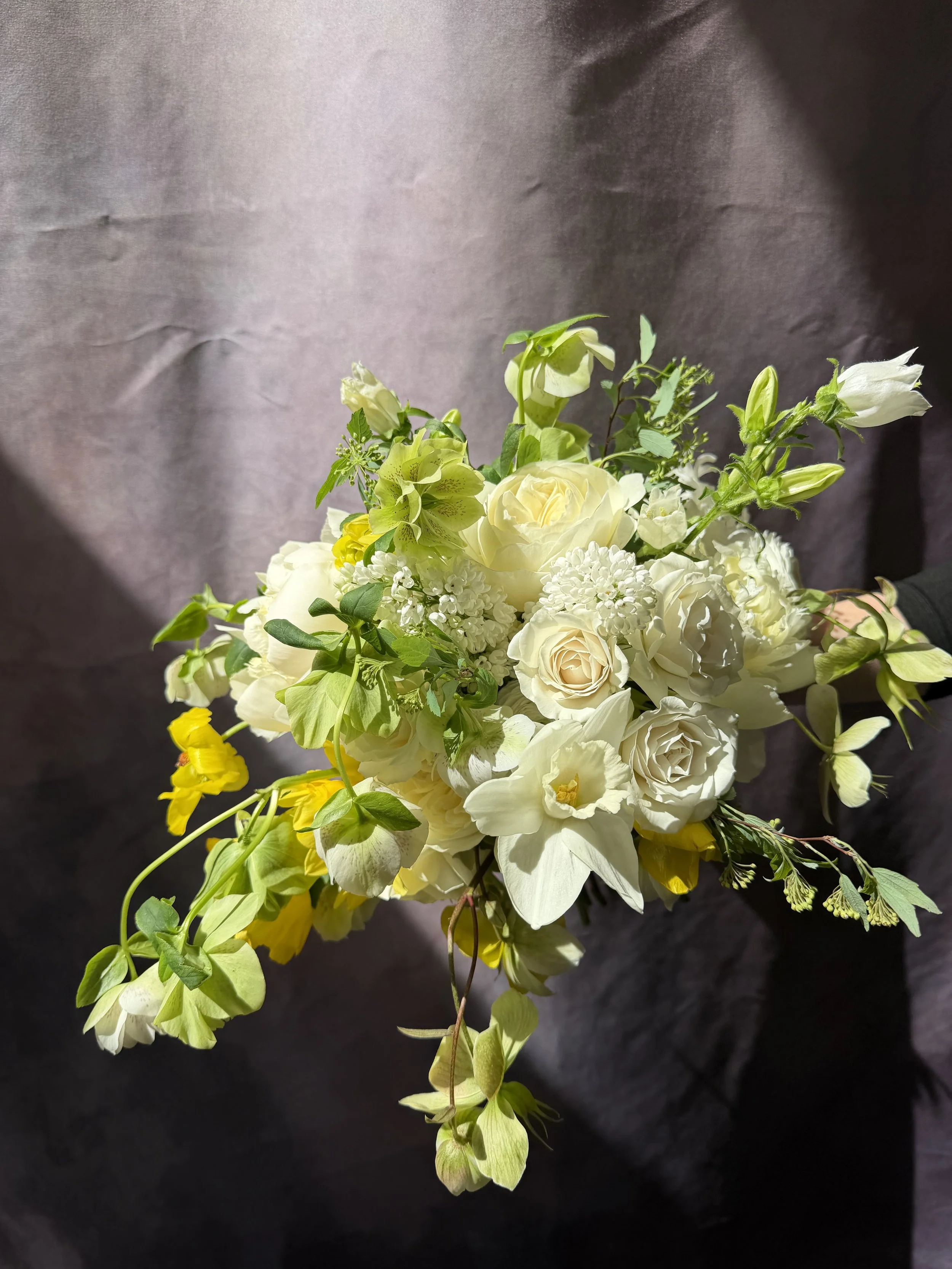 A bouquet of white and yellow flowers with green leaves, held against a dark background.