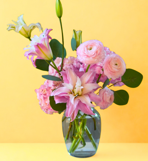 Pink and white flowers in a glass vase with green leaves on a yellow background.