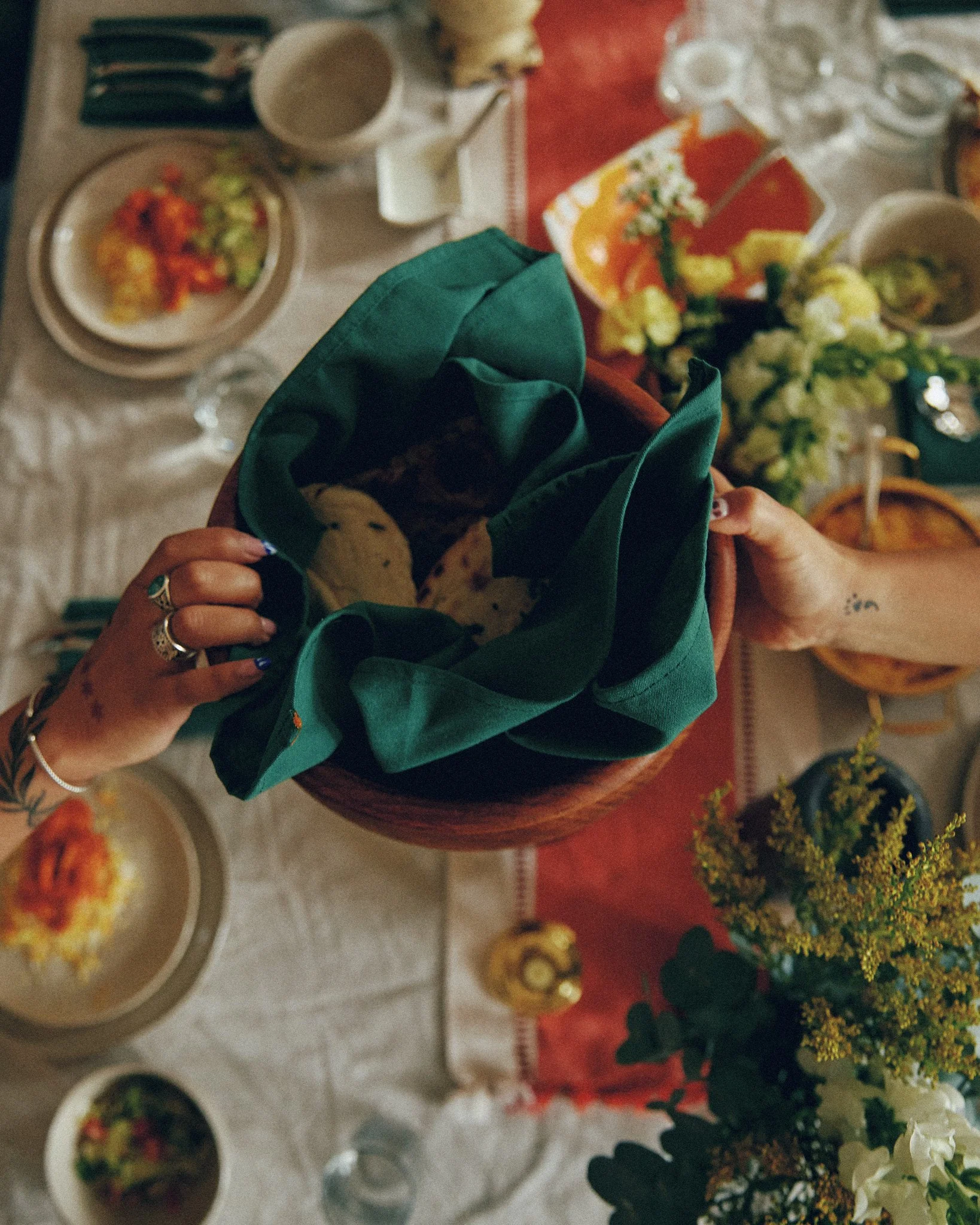 A top-down view of a table with various dishes and drinks, including a bowl of cream soup, a plate of salad, glasses of water, and a basket of bread, along with a person holding a plate with tortilla chips wrapped in a green napkin.