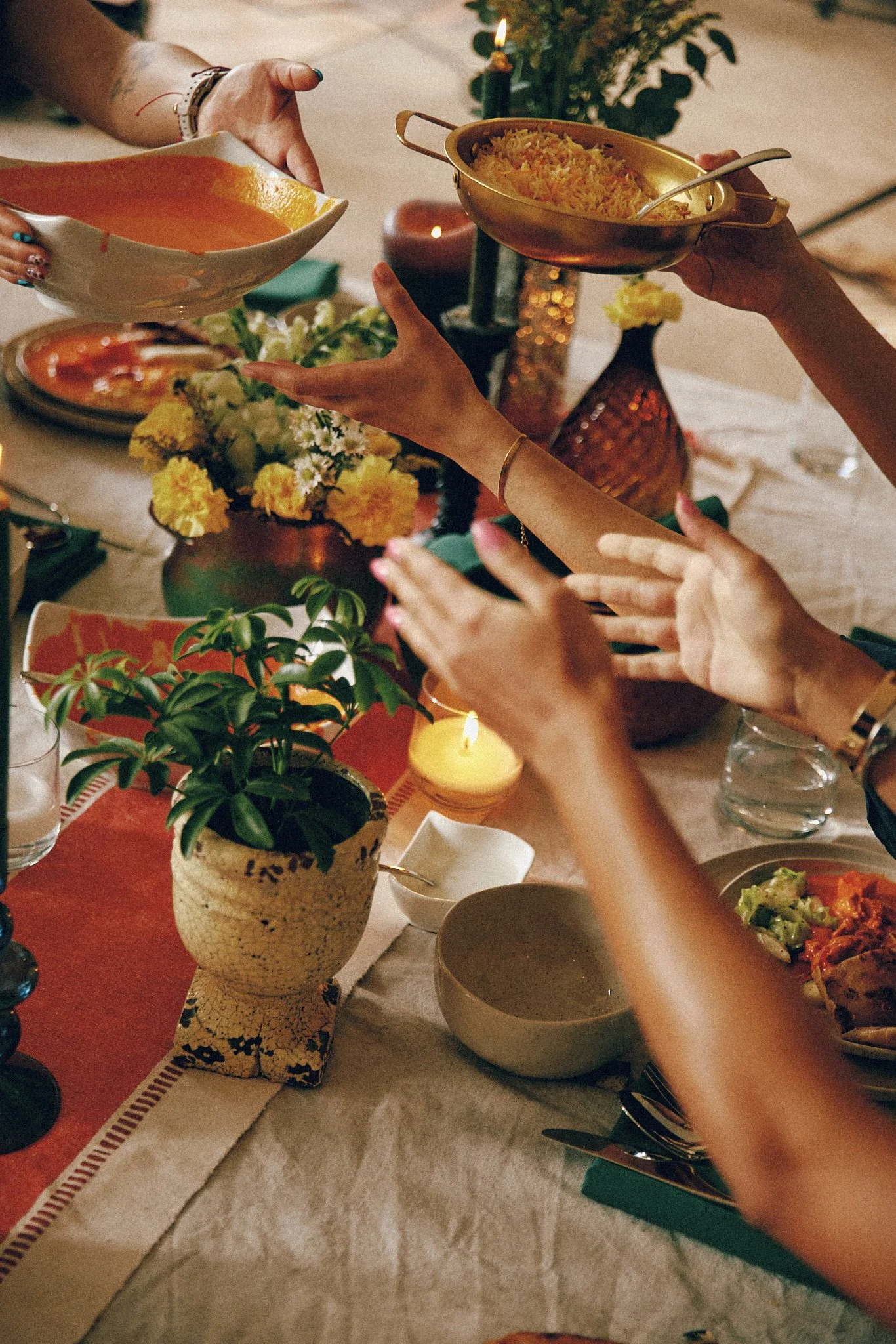 People serving rice and soup at a dinner table decorated with flowers, candles, and plants.