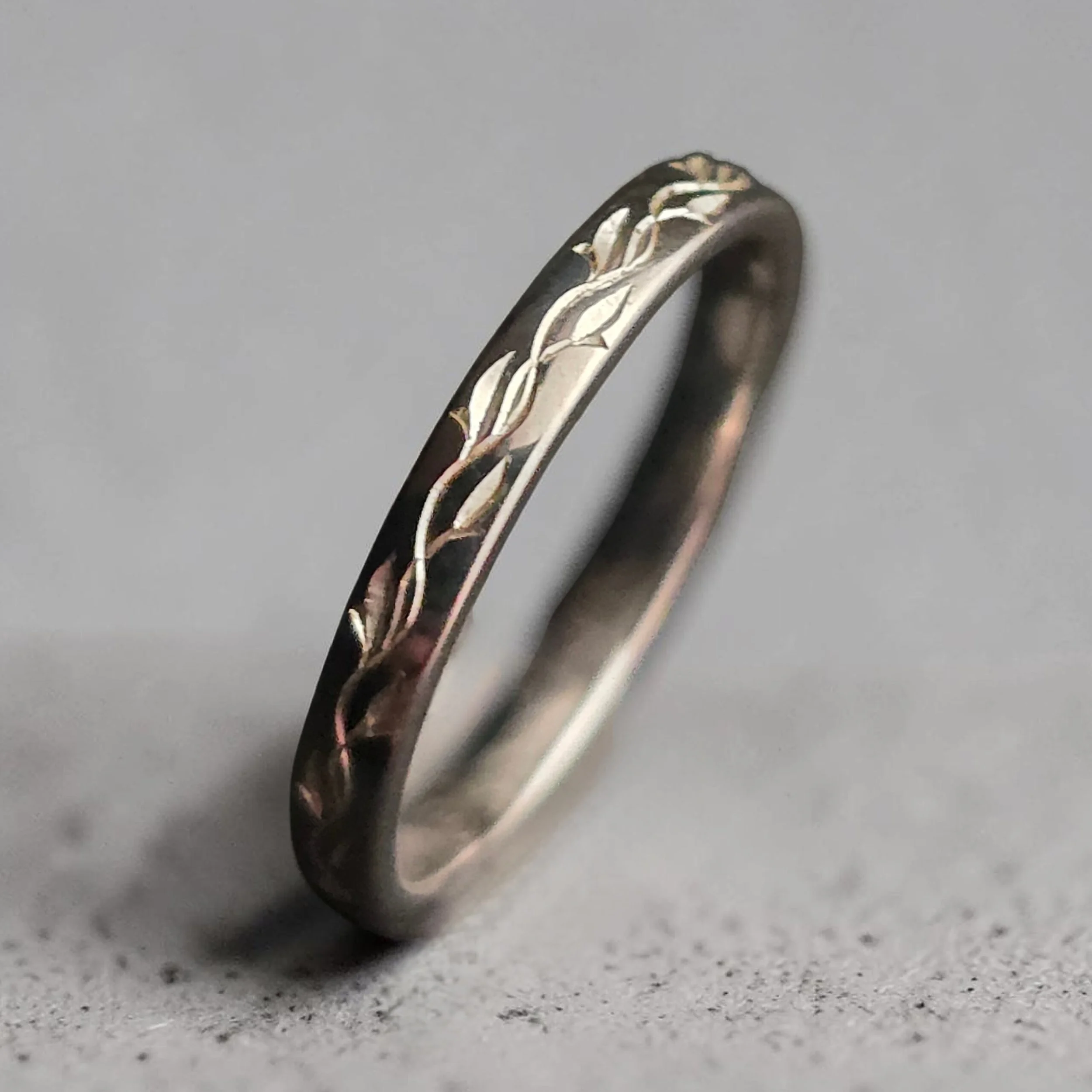 Close-up of a sterling silver wedding or engagement band featuring a unique bespoke botanical vine hand engraved pattern.