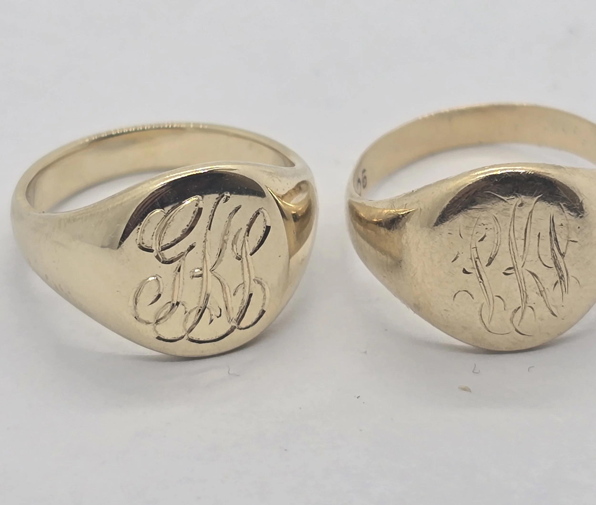 Close-up of two gold rings with hand engraved letter and monogram designs on a white background.