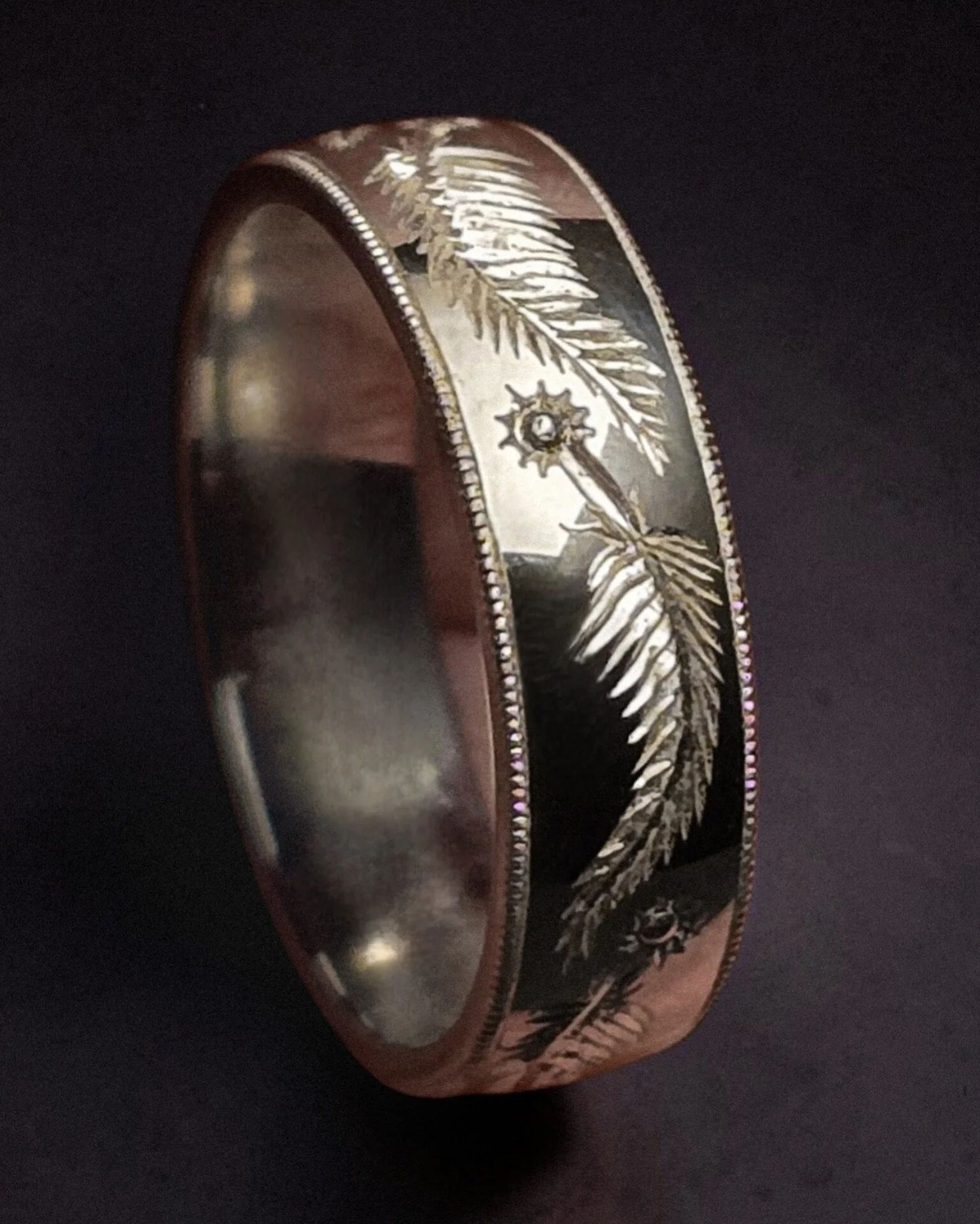 Close-up of a sterling silver wedding or engagement band featuring a unique bespoke feather hand engraved pattern.