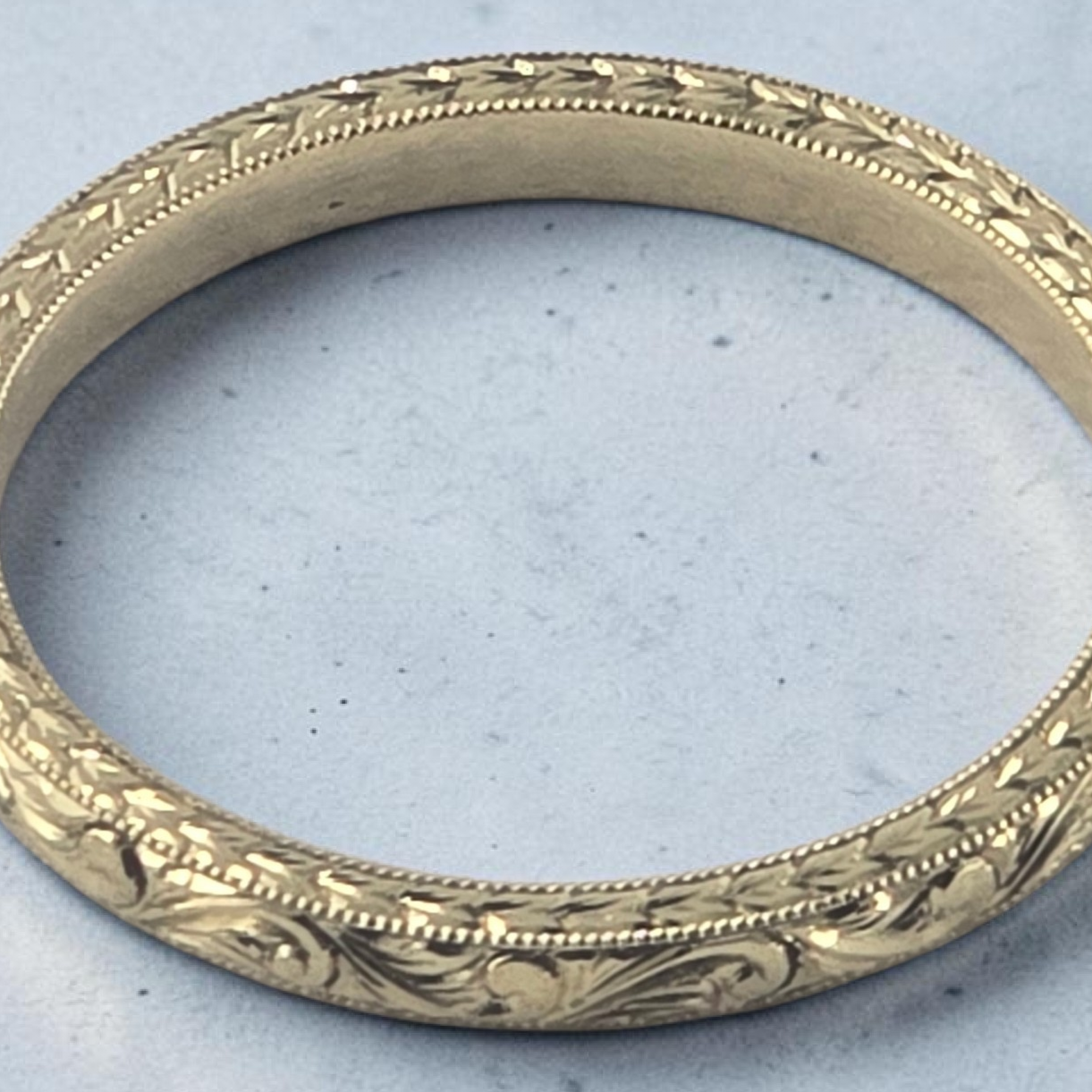 Close-up of a sterling silver wedding or engagement band featuring a unique bespoke feather hand engraved pattern.