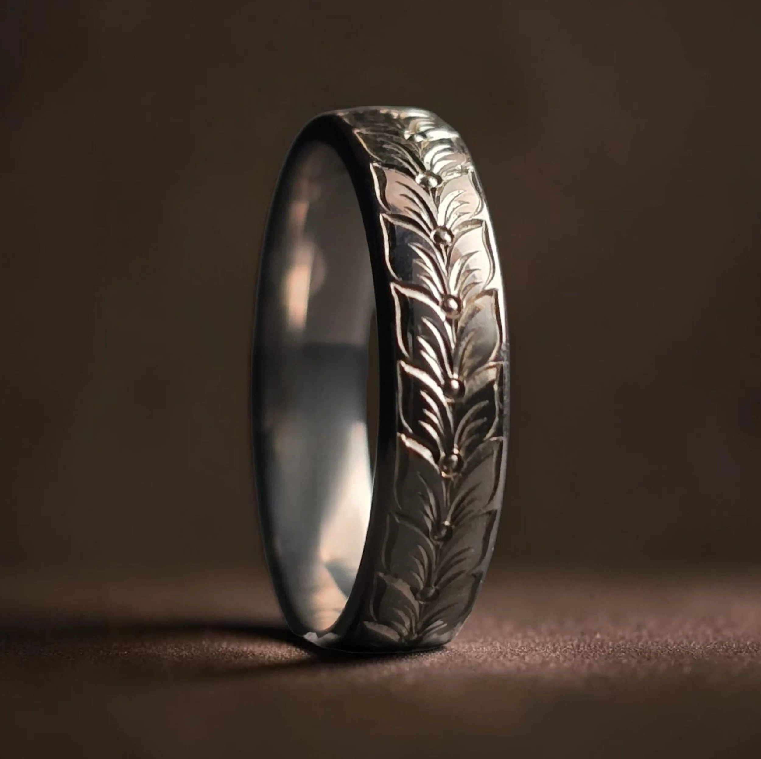 Close-up of a black wedding ring with a hand engraved botanical, vine, nature inspired pattern.