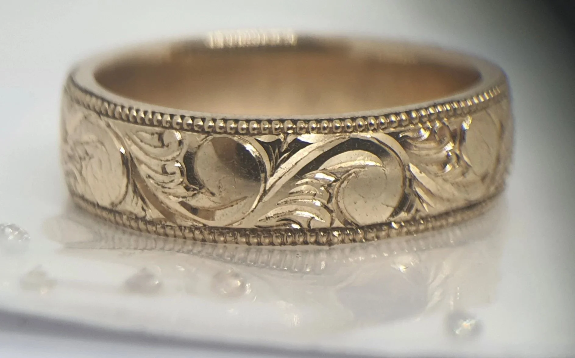 Close-up of a sterling silver wedding or engagement band featuring a unique bespoke botanical hand engraved pattern.