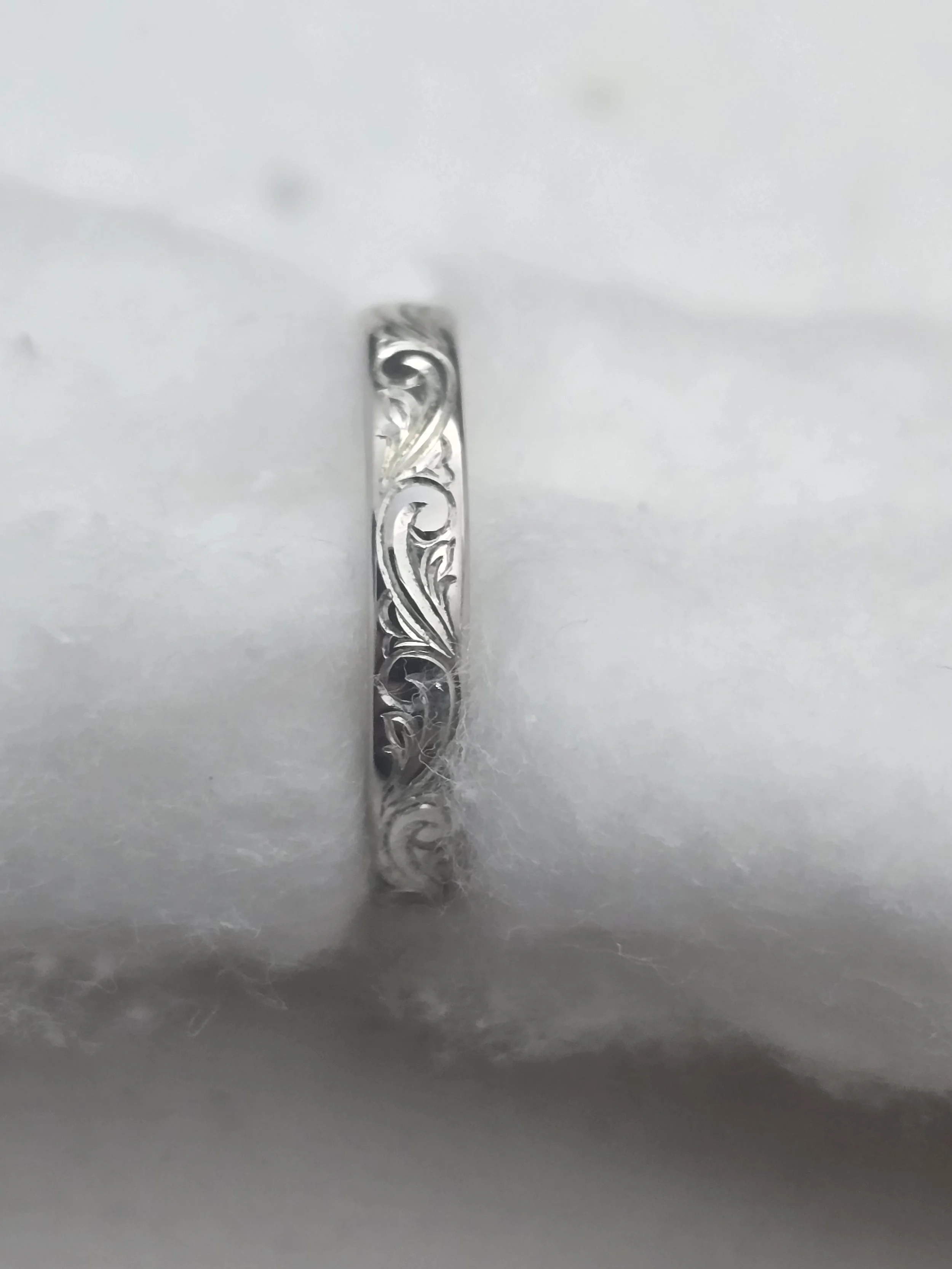 Close-up of a white gold wedding or engagement band featuring a vintage unique bespoke botanical hand engraved pattern.