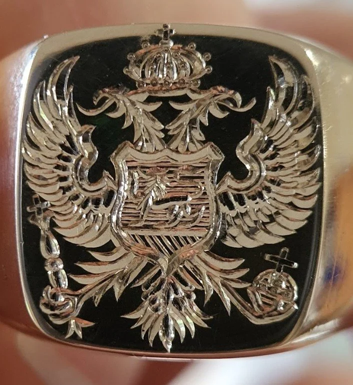 Gold expertly crafted hand engraved signet ring with a detailed double-headed eagle crest, featuring a crown on top and a shield with a bird emblem, symbolizing national or heraldic significance.